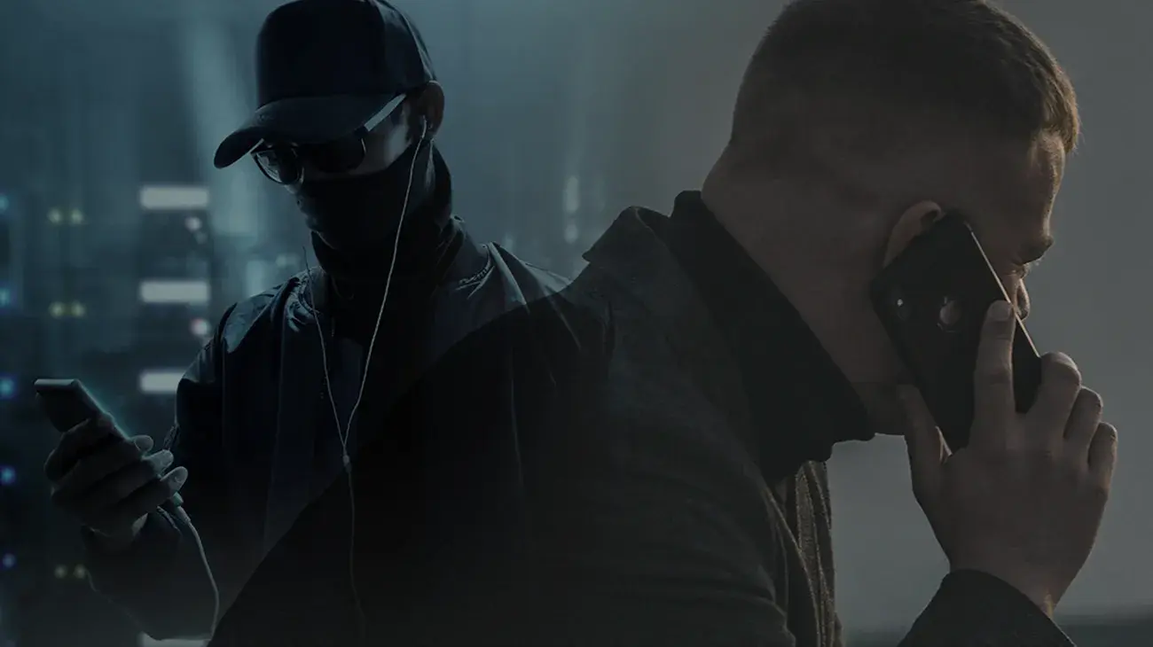 Two men in dark garments shrouding their faces on mobile phones. 