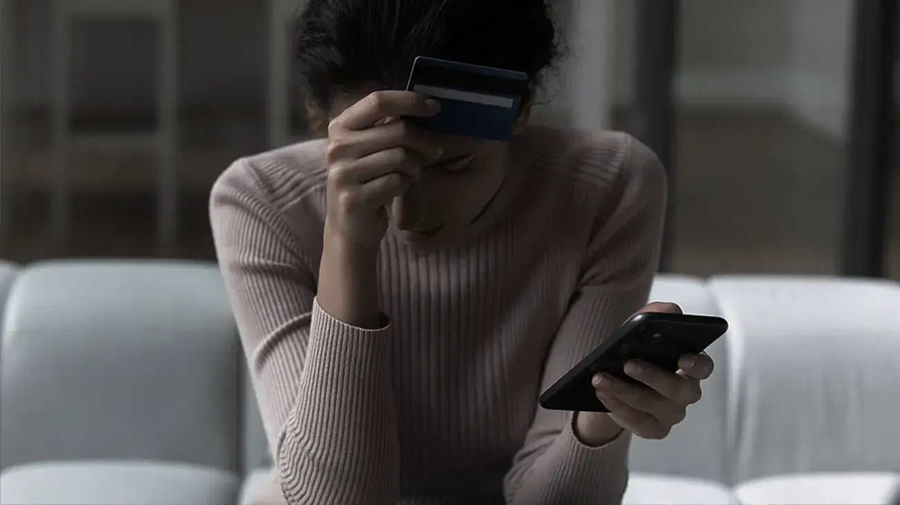 A woman upset and leaning over in a sitting position with a mobile phone in her hand