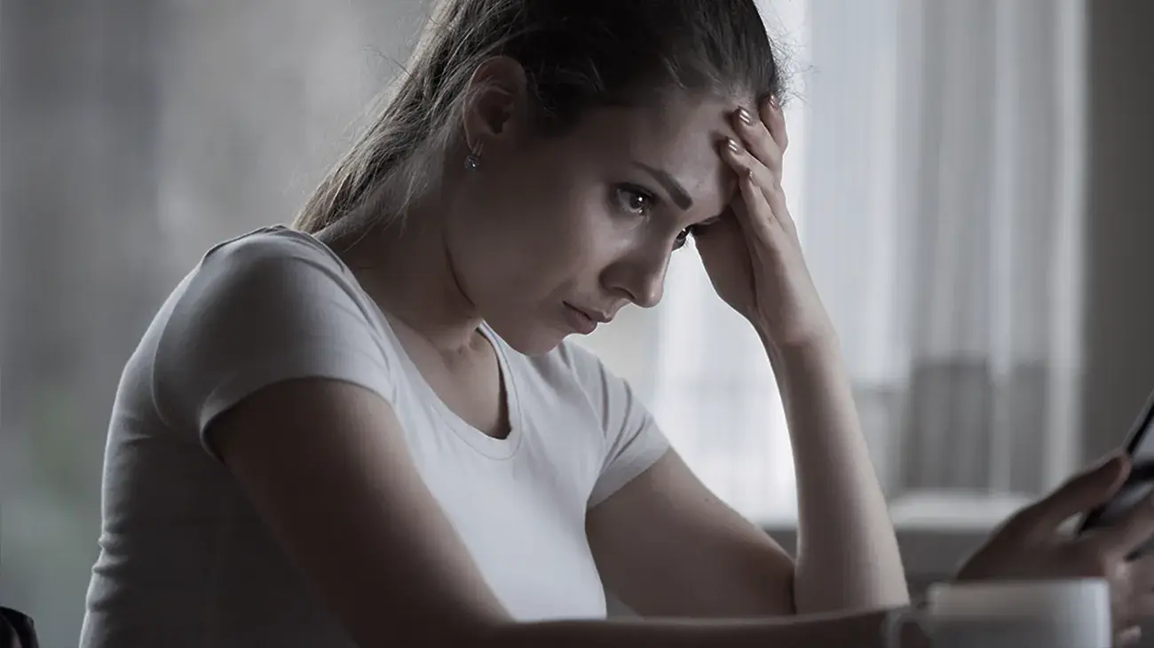 A young woman with her head leaning on her hand looking concerned at her mobile phone