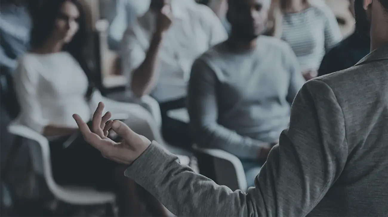 A person with long sleeves presenting to an audience with their arm outstretched and interested audience members