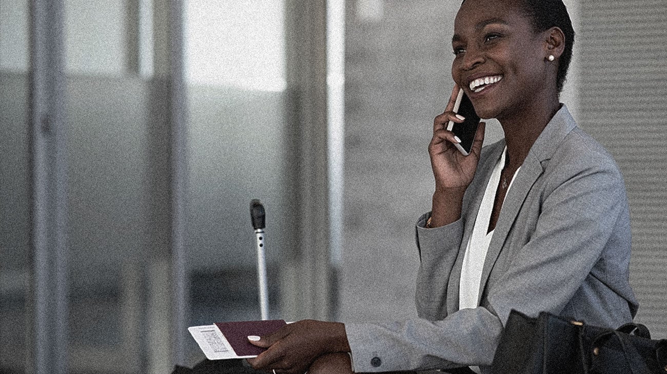 A black lady talking on the phone with a large smile at her work desk